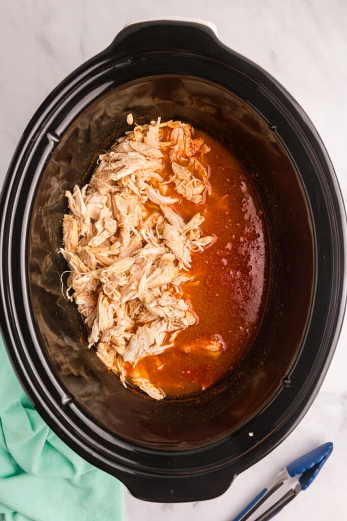 Shredded chicken and buffalo broth mixture in a slow cooker.