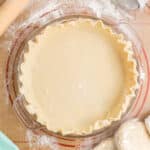 Unbaked pie crust in a dish with wrapped dough discs beside it.