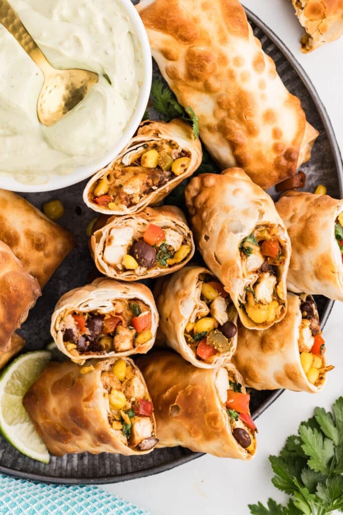 Platter of halved Southwestern egg rolls with a bowl of creamy green dip.
