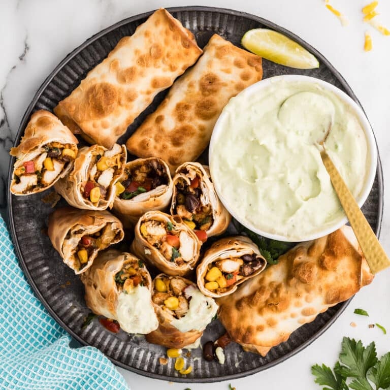 Golden brown egg rolls with dipping sauce on a round tray.