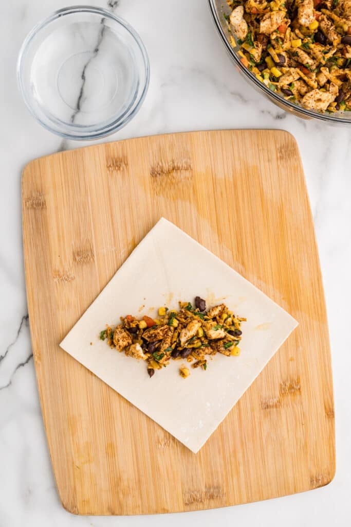 Egg roll wrapper with filling on a wooden board.