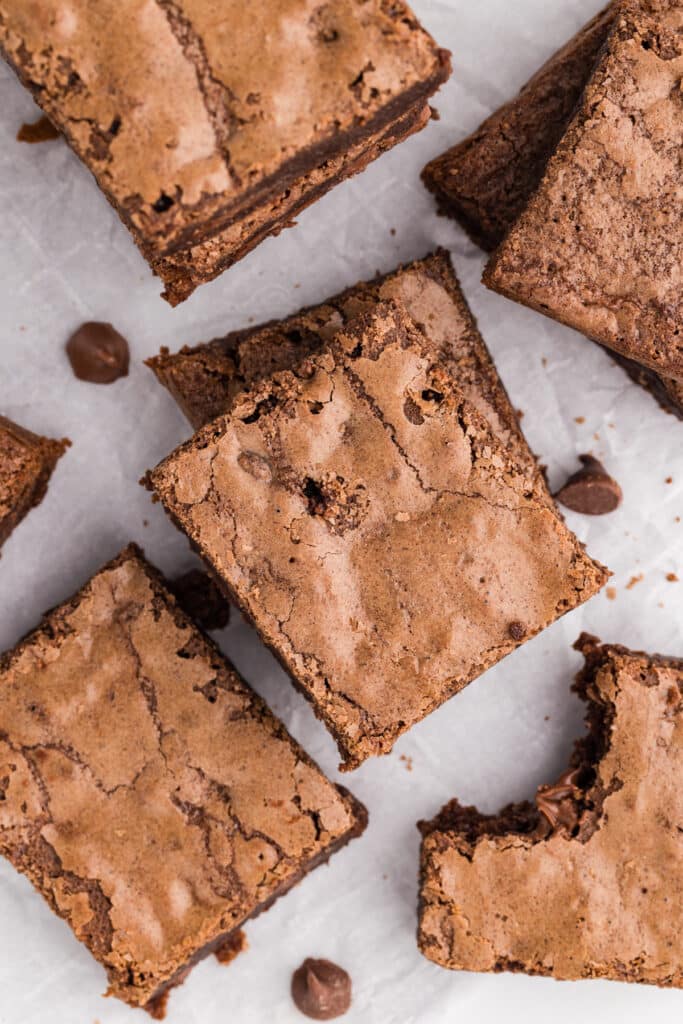 Fudgy brownies on parchment with one piece missing a bite.
