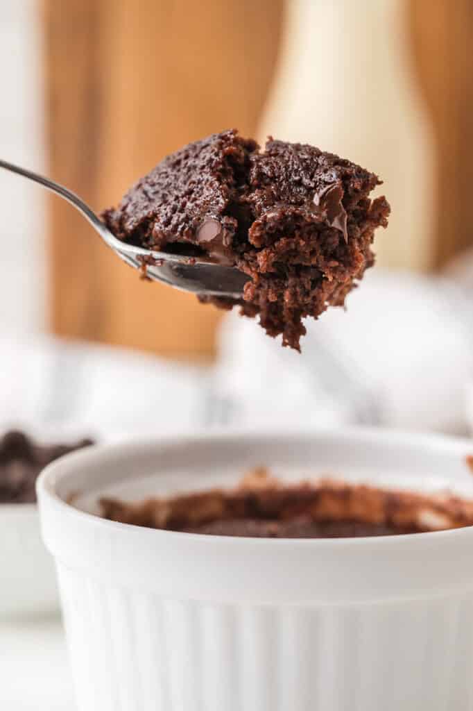 Spoon lifting a bite of brownie from a white ramekin.