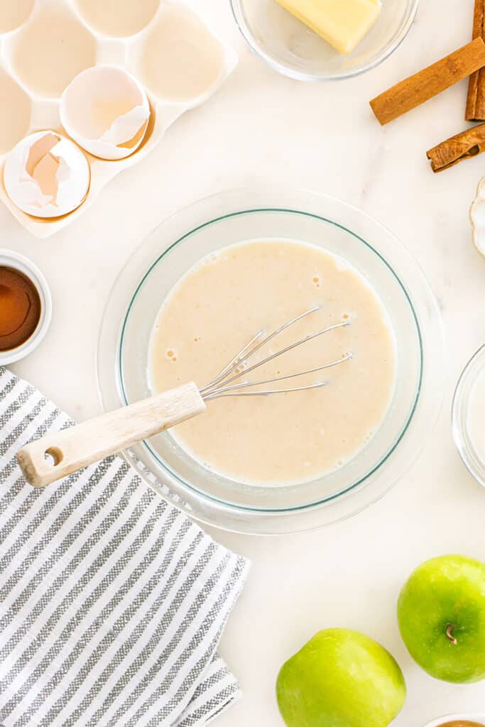 Wet batter mixture in a glass bowl with a whisk.