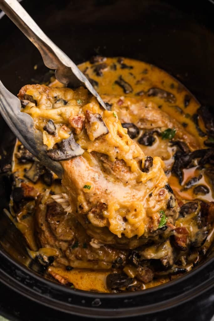 Cheesy chicken being lifted from a slow cooker with tongs.