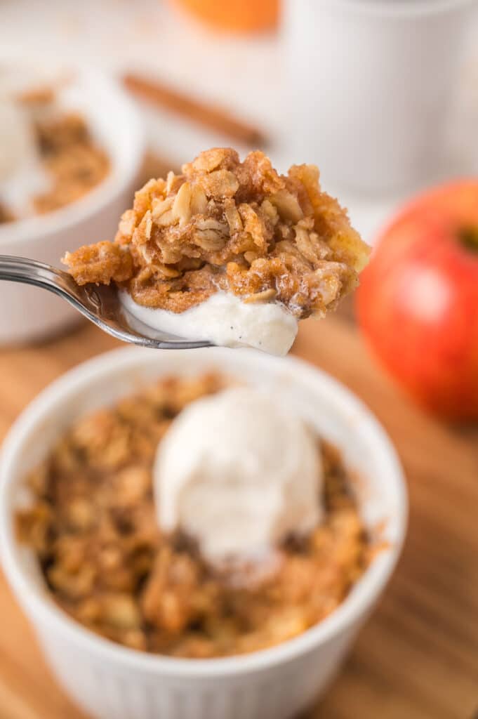 A spoonful of apple crisp with a scoop of melting vanilla ice cream in the background.