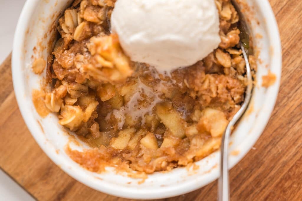 Partially eaten apple crisp with melting ice cream in a white ramekin.