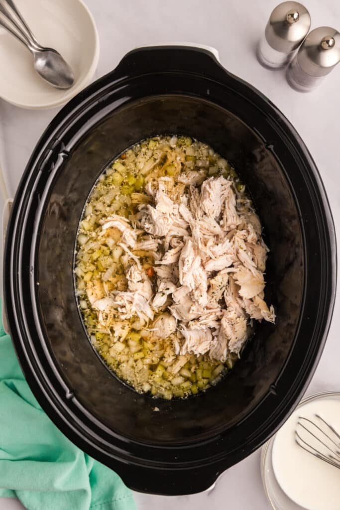 Shredded cooked chicken added back into the slow cooker with broth and vegetables.
