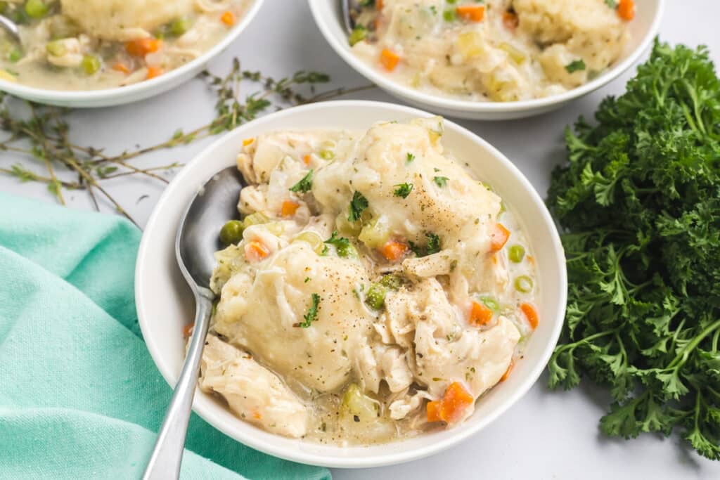 Three bowls of creamy chicken and dumplings with peas and carrots.