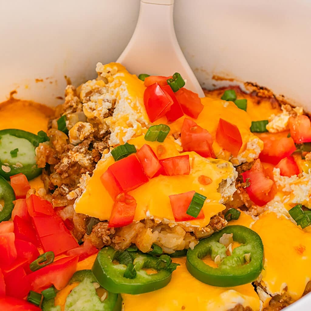 Close-up of a cheesy casserole topped with diced tomatoes and sliced jalapeños.