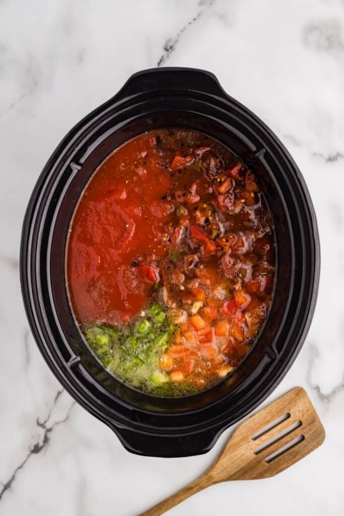 Ingredients for stuffed pepper soup layered in a slow cooker.