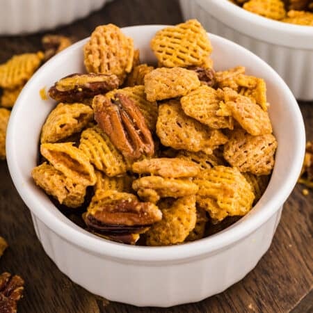 Bowl of butter pecan snack mix on a wooden board.