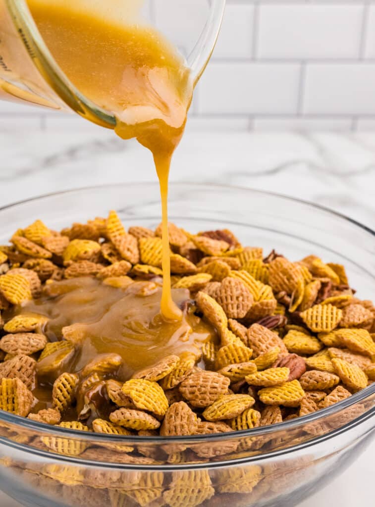Caramel sauce being poured over cereal and pecans in a glass bowl.