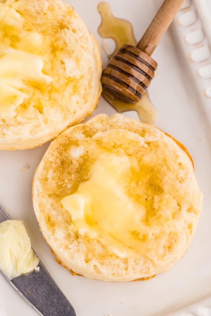 A halved biscuit with melted butter and honey next to a wooden honey dipper.