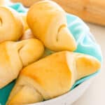Freshly baked crescent rolls piled in a bowl lined with a turquoise cloth.