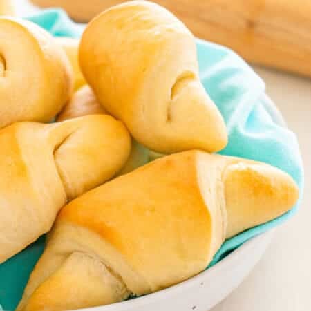 Freshly baked crescent rolls piled in a bowl lined with a turquoise cloth.