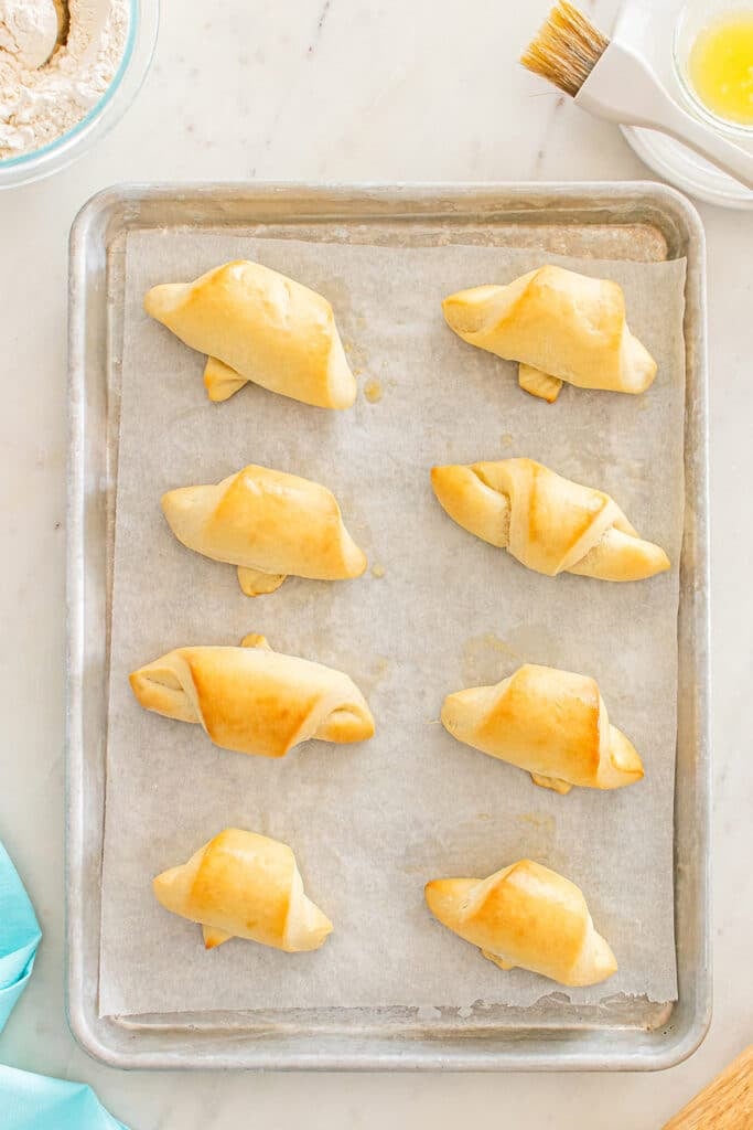 Baked crescent rolls arranged on a parchment-lined sheet pan.