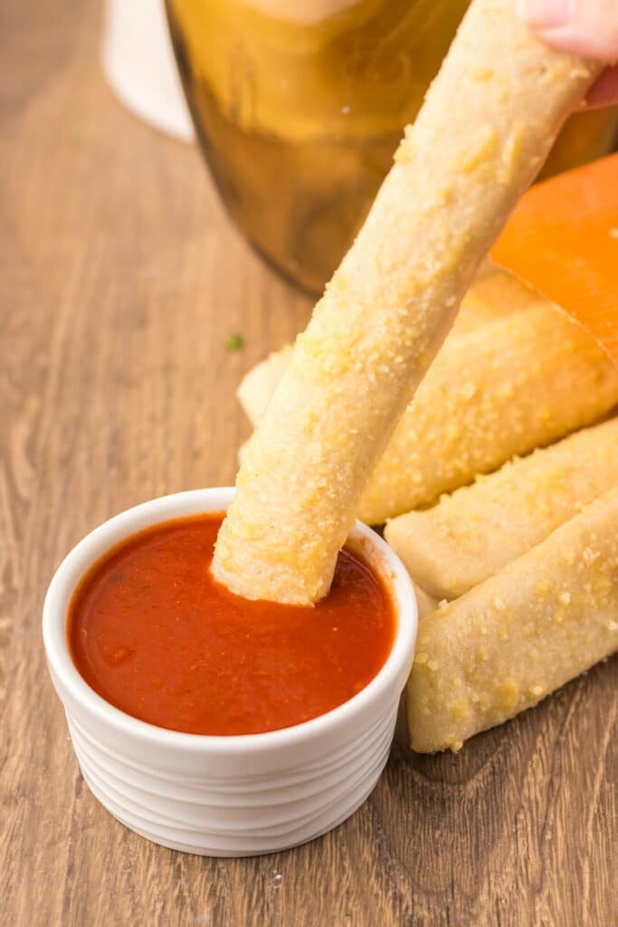 Breadstick being dipped into marinara sauce.