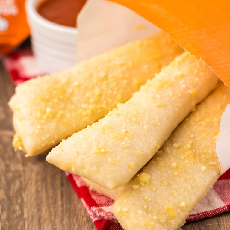 Breadsticks in an orange paper sleeve next to marinara sauce.