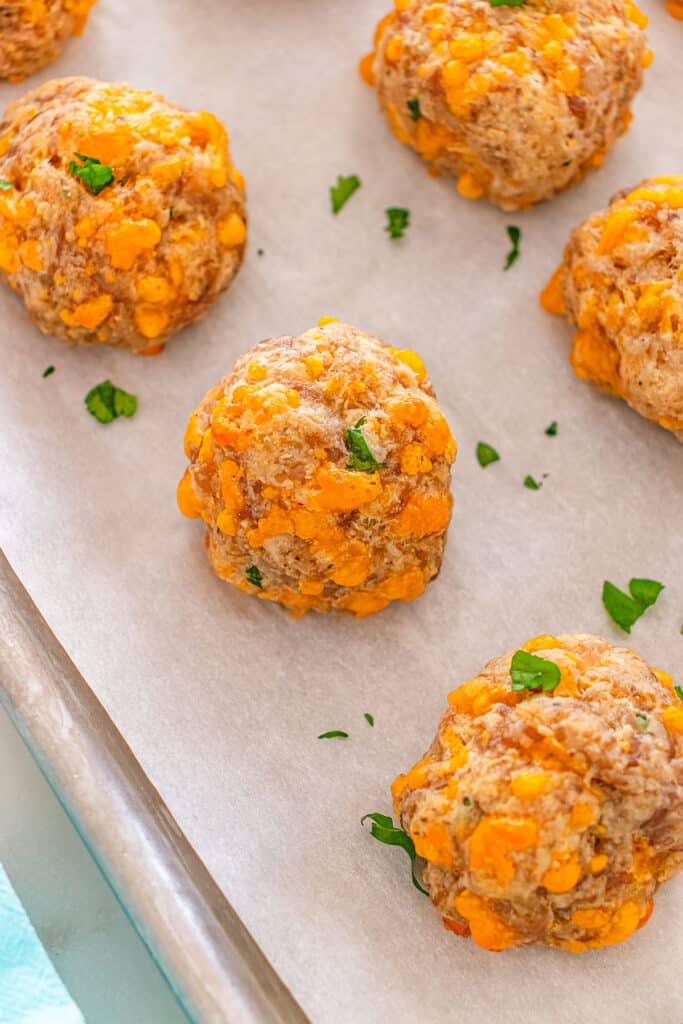 Baked sausage balls with melted cheese on a parchment-lined baking sheet.
