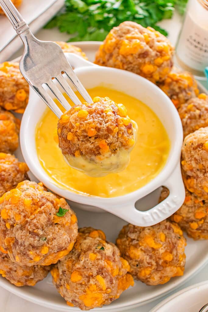 A fork holding a sausage ball dipped into yellow cheese sauce.