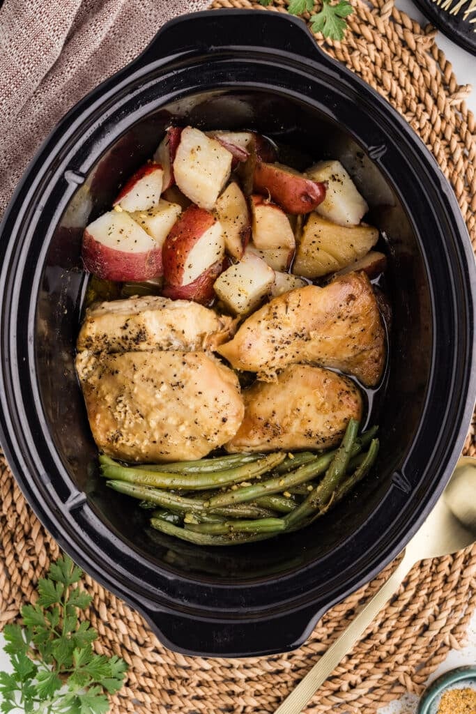 Cooked chicken breasts, potatoes, and green beans in a slow cooker.