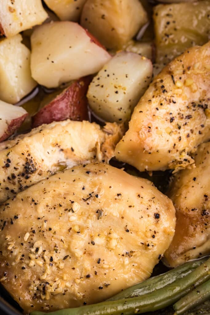 Close-up of cooked chicken breasts with red potatoes and green beans.