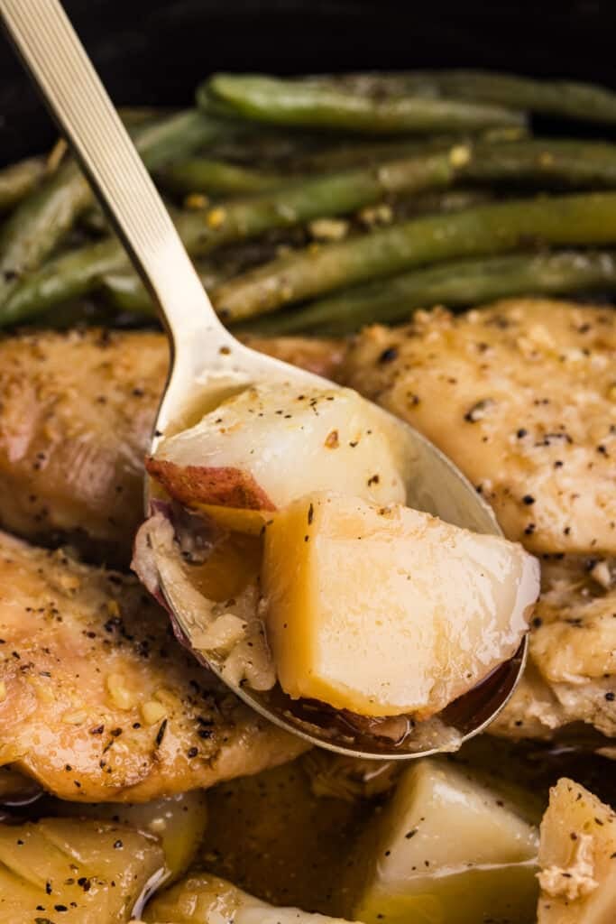 Spoon lifting potatoes from slow cooker with chicken and green beans.