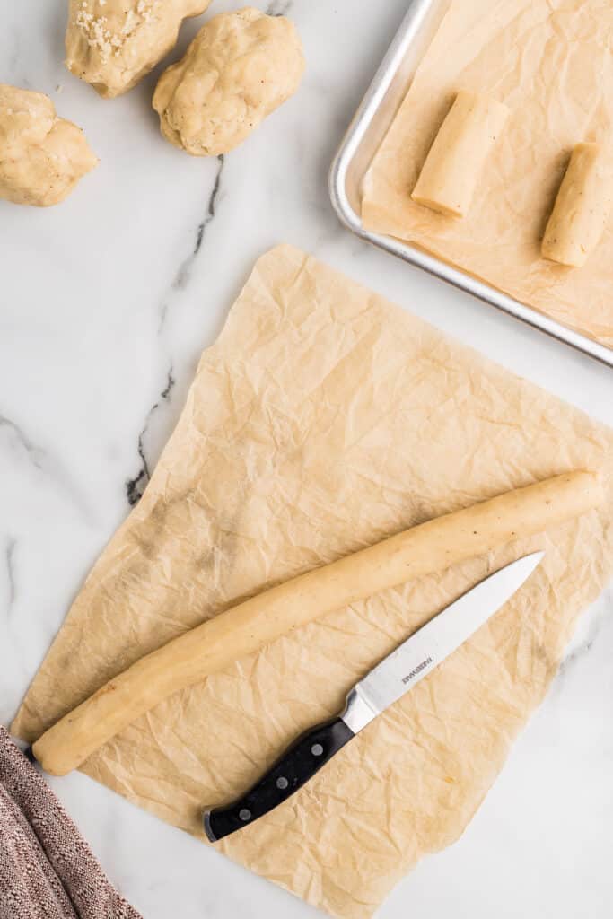 Cookie dough rolled into logs on parchment with a knife nearby.