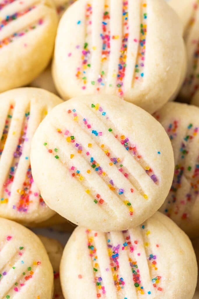 Close-up of round shortbread cookies topped with rainbow sprinkles.