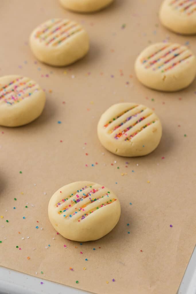 Unbaked round cookie dough topped with rainbow sprinkles on parchment paper.