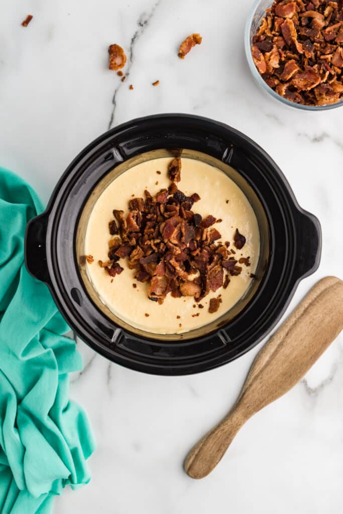 Slow cooker filled with creamy cheese dip topped with chopped crispy bacon.