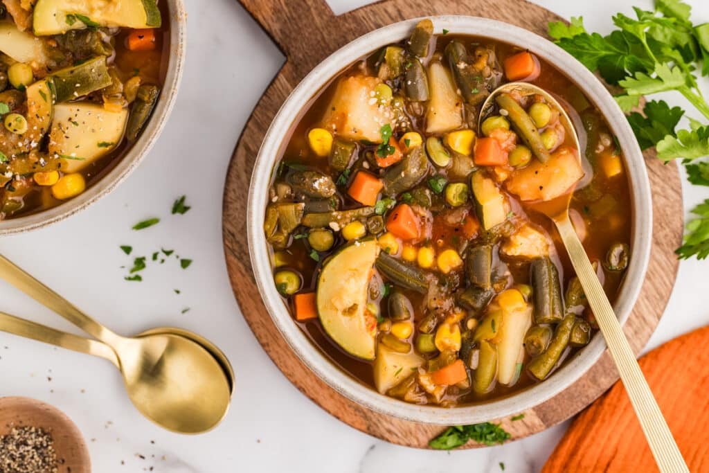 overhead shot of a bowl of chunky vegetable soup with a gold spoon.