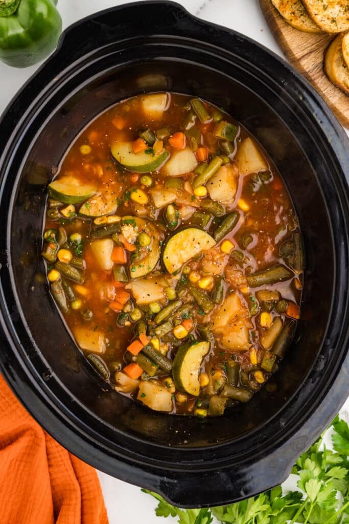 Vegetable soup cooking inside a black slow cooker.