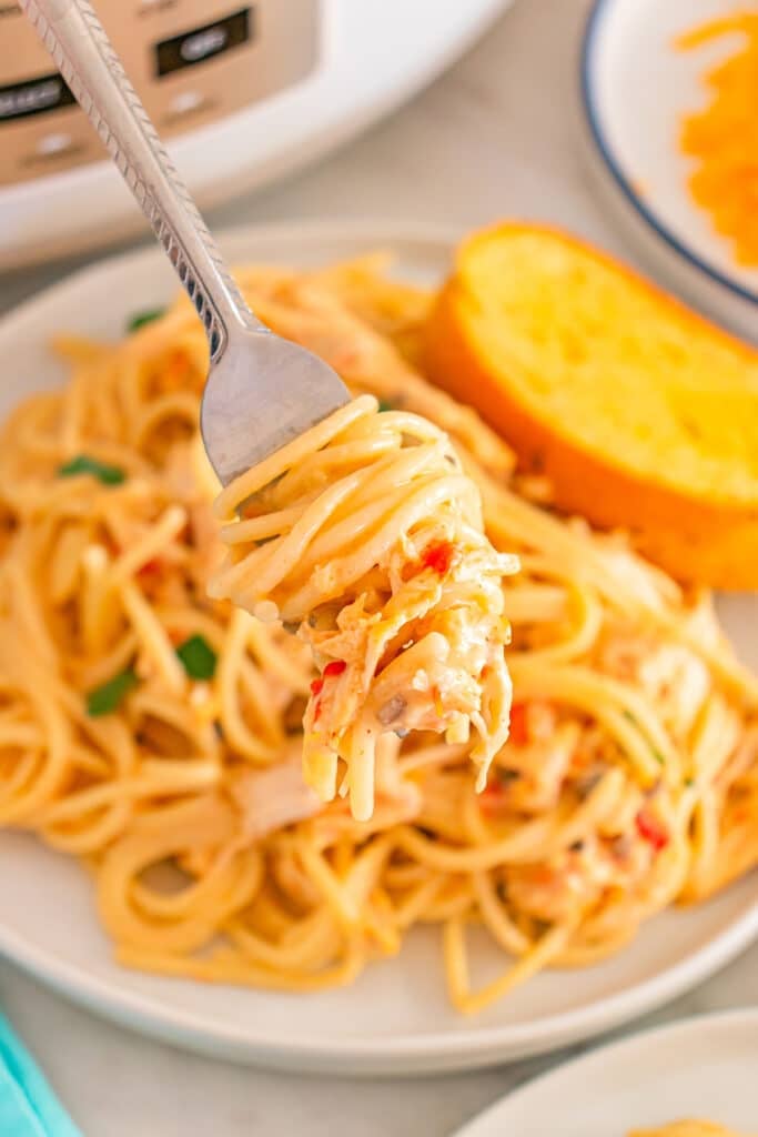 Fork lifting creamy chicken spaghetti with garlic bread in background.