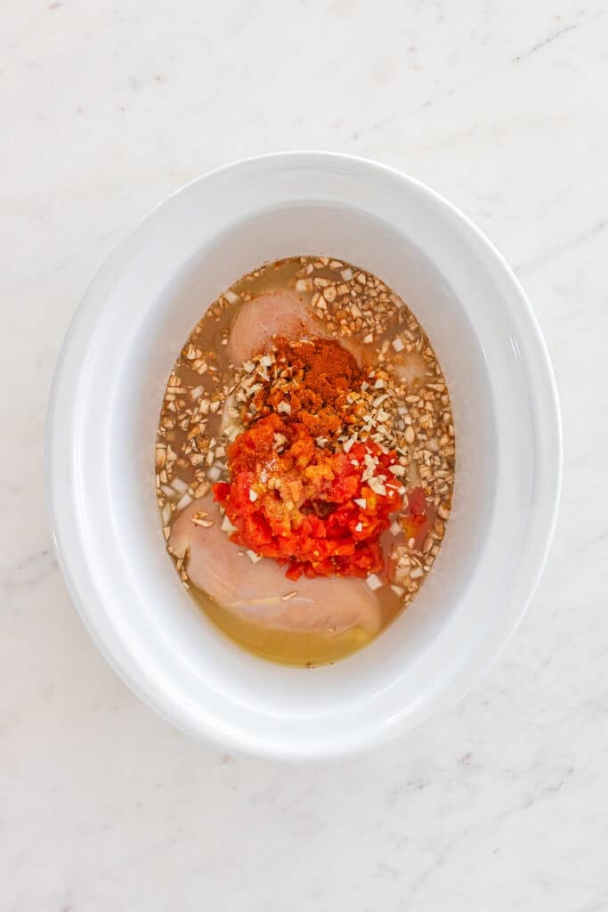 Raw chicken breasts in slow cooker with diced tomatoes, mushrooms, and seasonings.