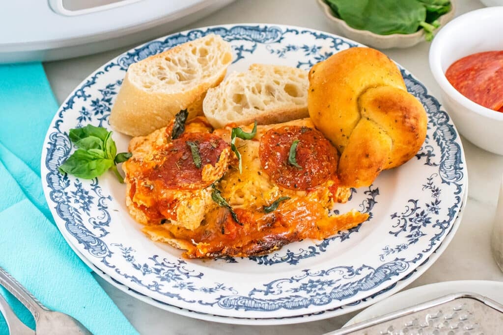 Slow cooker pizza dip served with bread and garlic knots on a plate.
