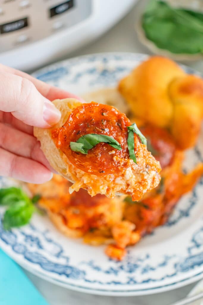 Hand holding bread topped with cheesy pizza dip and pepperoni.