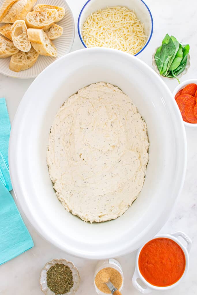 Creamy pizza dip base spread in a crockpot before adding toppings.