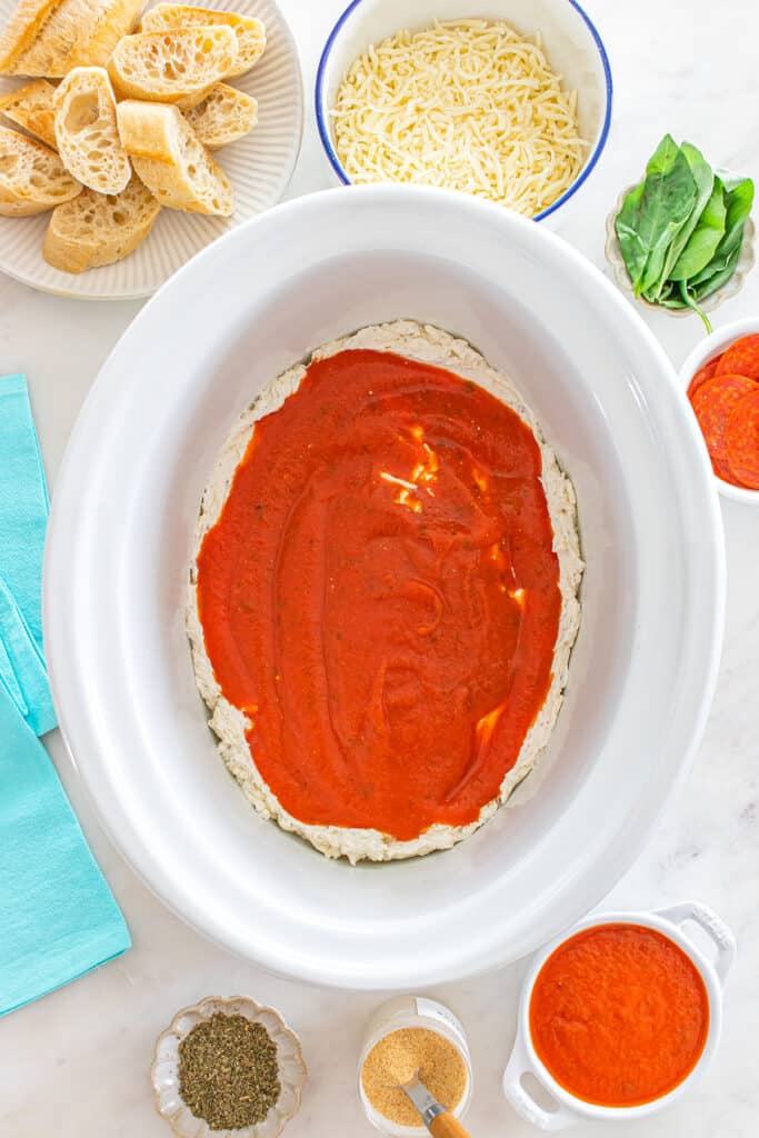 Pizza dip in crockpot topped with marinara sauce before cooking.